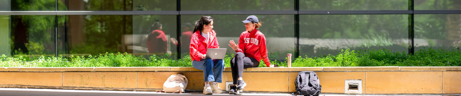 Two people converse in front of a glass paneled building